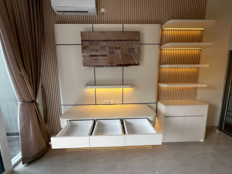 Backdrop TV putih dengan kabinet bawah dan rak pajangan LED.