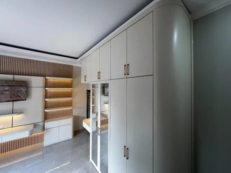 Wardrobe custom putih dengan pintu cermin dan kabinet penyimpanan atas.