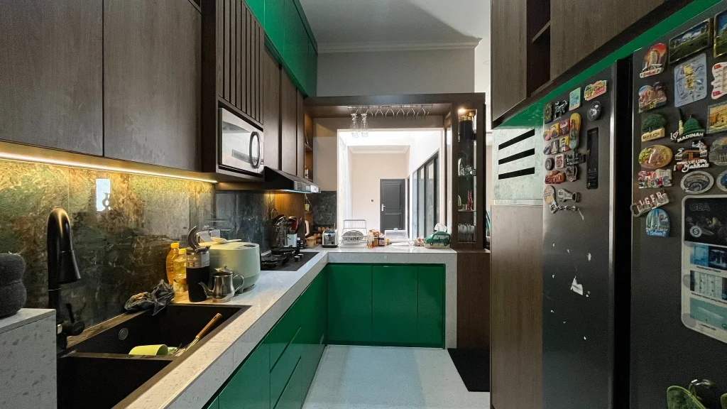 Kitchen set berbentuk L dengan kabinet hijau emerald dan motif kayu.