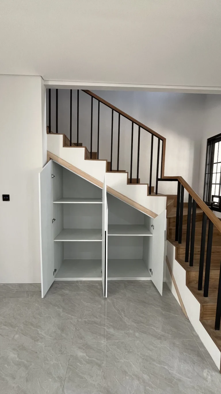 Detail rak terbuka dan kabinet custom di bawah tangga.