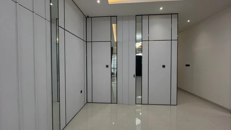 Lemari pakaian tinggi dengan pintu solid dan panel cermin.